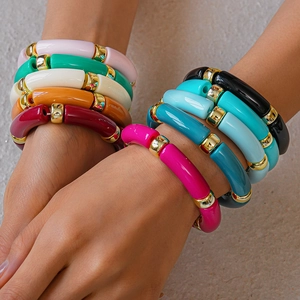 Dettaglio di braccialetti colorati in resina acrilica con perline dorate al polso