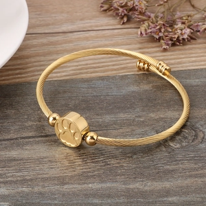 Detail of a gold cable wire bangle featuring a paw print charm on a rustic wood background