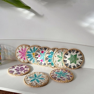 Detailed view of handcrafted round rattan coasters with colorful shell mosaic flower patterns