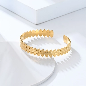 Detailed close-up of textured gold cuff bracelet with leaf-like oval patterns on a white stone