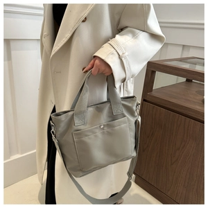 Detalle de bolso tote gris de nailon con asas de cincha y correa ajustable para hombro