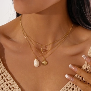Close-up of triple-layered gold necklace with starfish and white shell charms on neck