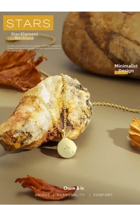 Detail of gold coin necklace with starburst design displayed on natural stone and leaves