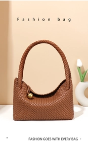 Detail of hand-woven brown leather tote bag featuring a decorative gold sphere charm
