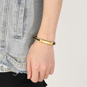 Detail view of a men's black woven bracelet with gold metal plate on wrist