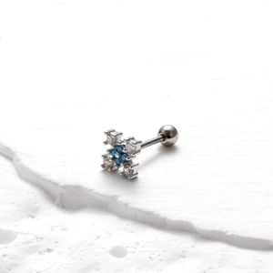 Macro detail of silver barbell earring with blue zircon flower on a white stone base