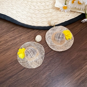 Detail of raffia straw hat earrings with small yellow flower accents on wood background