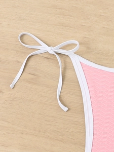 Macro view of pink smocked texture fabric and white side-tie bow on bikini bottom