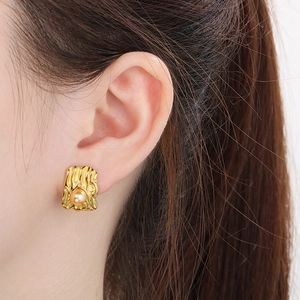 Close-up of gold irregular wrinkled texture square earring with a centered pearl inlay
