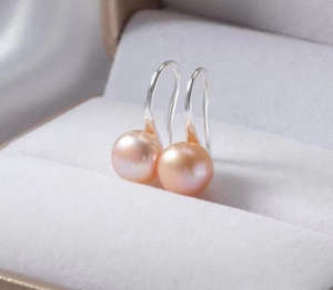Macro shot of pink pearl earrings with silver hooks in a grey velvet jewelry box