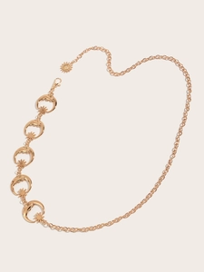 Détail d'une chaîne de taille dorée avec pendentifs lune et étoile sur fond crème