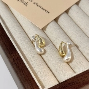 Detail view of two-tone gold and silver teardrop stud earrings on a beige velvet jewelry box