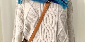 Macro detail of cream cable knit sweater texture with blue plush scarf and leather strap