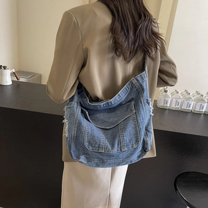 Grand sac à bandoulière minimaliste en jean bleu avec bords effilochés porté par un modèle