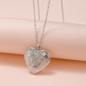Detailed view of silver heart locket pendant with vintage floral engraving on pink stand