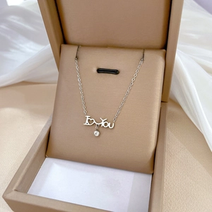 Detail of silver heart and letter pendant with zircon on a beige jewelry box