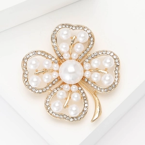 Elegant gold clover brooch with pearls and rhinestones on a white geometric background