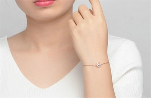 Rose gold chain bracelet with a floral charm and centered heart zircon on model wrist
