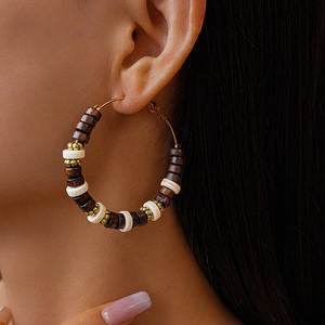 Gros plan d'une boucle d'oreille créole dorée avec perles marron et blanches