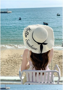 Detail of wide-brim straw hat with black ribbon and Hello Sunshine embroidery by the sea