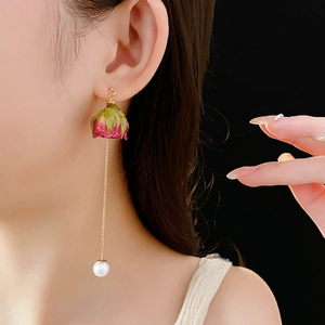Vue macro de longues boucles d'oreilles avec boutons de rose et pendentifs perles blanches