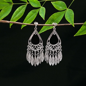 Detailed close-up of ethnic silver leaf tassel earrings hanging on a green branch