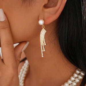 Close-up of golden pearl earrings with sparkling rhinestones and geometric fringe design