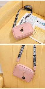 Close-up of pink embossed crossbody bag featuring a cat charm and wide printed strap
