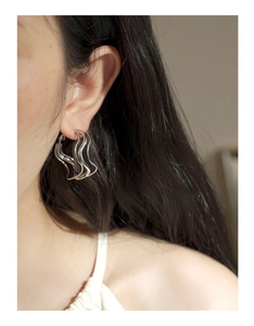 Close-up of minimalist silver twisted hoop earrings worn by a model in a natural setting