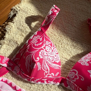 Dettaglio di un top bikini rosa a fiori con bordi arricciati e spalline su telo da mare