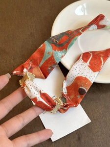 Close-up of orange silk scarf hair tie with elegant art print and gold metal buckle