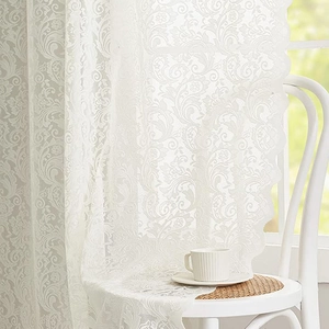 White lace curtain with floral patterns and wavy edges hanging in a sunny cozy room