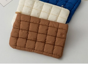 Detailed view of quilted puffer clutch bags in brown, beige, and blue with gold zippers