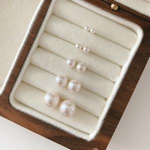 Set of 5 pairs of white pearl stud earrings in various sizes on a velvet display