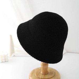 Détail du crochet fait main d'un chapeau bob noir sur un support en bois clair