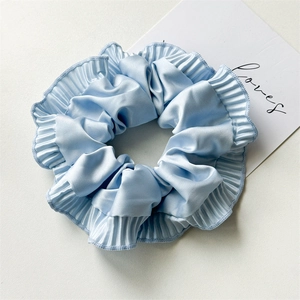 Detail of light blue satin scrunchie with pleated edges and soft silky sheen texture