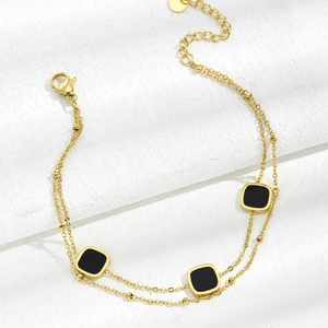 Detailed macro view of a double-layered gold bracelet featuring three black square pendants
