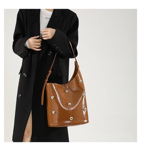 Close-up of brown bucket bag with metal studs and adjustable strap on black blazer
