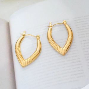 Macro detail of V-shaped 18K gold-plated titanium earrings with textured sunburst engraving