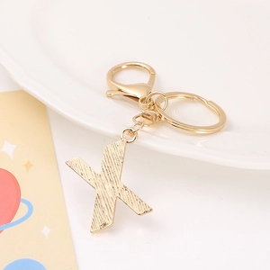 Detail of golden metal letter X keychain with textured finish and lobster clasp