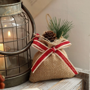 Linen Christmas gift bag with pine cone and bow decoration on cozy winter wood background