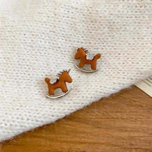 Dettaglio dei orecchini a forma di cavallo a dondolo marrone con zirconi su maglione