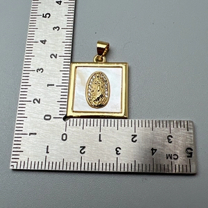 Macro shot measuring the gold religious square pendant with shell inlay and crystals