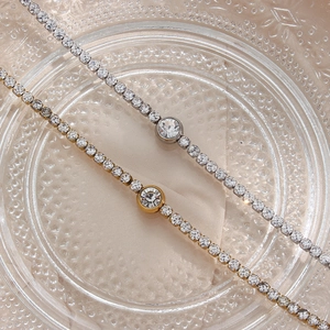 Close-up of gold and silver tennis bracelets with round zircon on glass tray