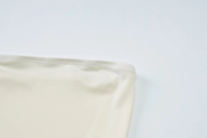 Detailed close-up of double-stitched hem and knit fabric texture on cream off-shoulder dress