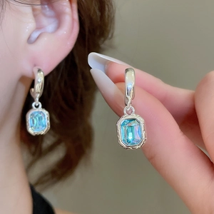 Detailed macro view of silver hoop earrings featuring iridescent rectangular blue gems