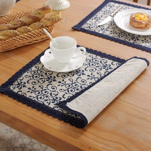 Close-up of linen table mat featuring blue floral patterns and intricate crochet edges
