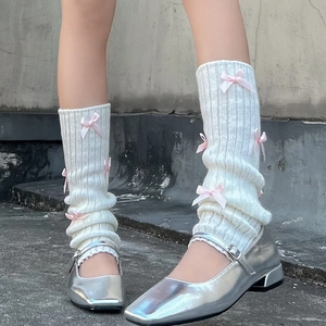 Gros plan de jambières en tricot côtelé blanc avec nœuds en soie rose et chaussures Mary Jane