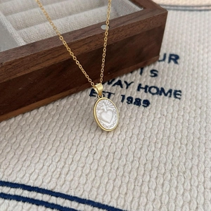 Detail of gold oval shell pendant with heart and cross on a wooden jewelry box