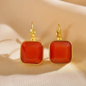 Detail view of square gold earrings with dark red stone on soft satin fabric background